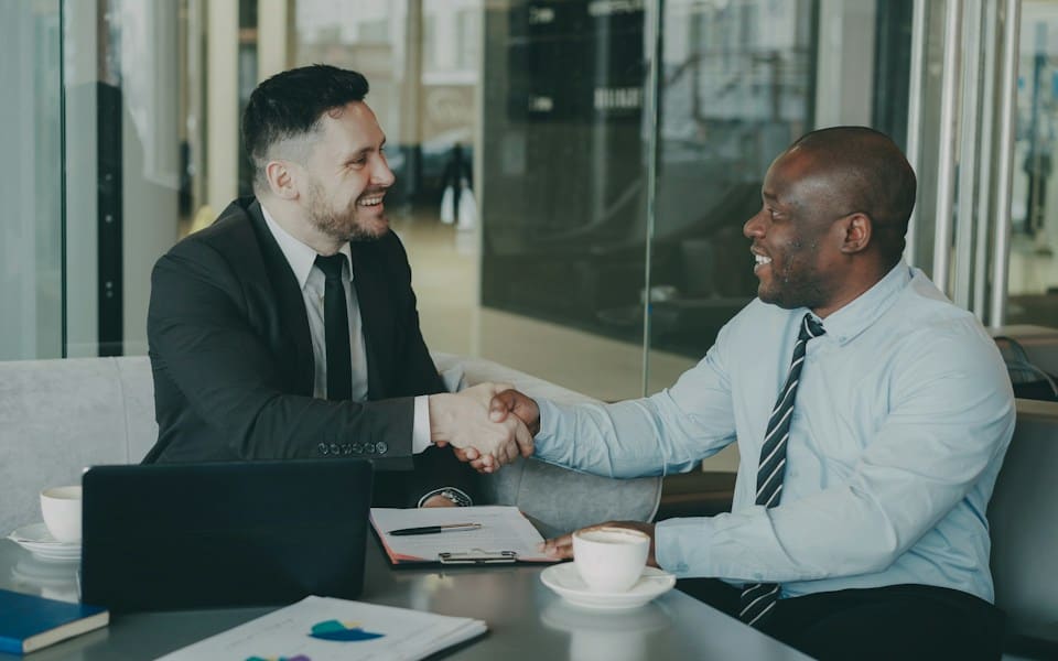 Two businessmen shaking hands across a meeting table