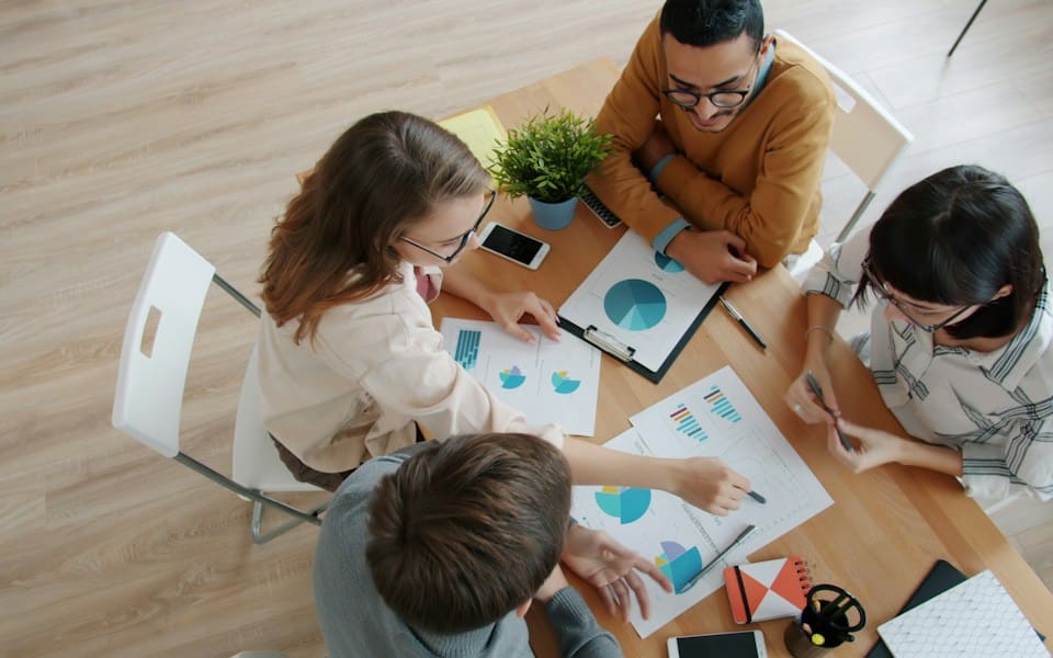 A team reviewing printed charts around a table, seen from above