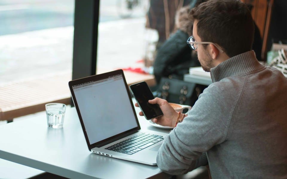 A man working on his laptop and phone at a café window